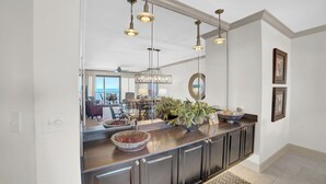 A modern kitchen with dark cabinetry, a large island with a bowl and plants, pendant lighting, and a view into the dining area.