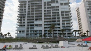 A high-rise hotel with multiple balconies and a beach area with sun loungers.