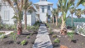 A white house with a central walkway surrounded by various plants and a fenced area.