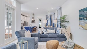 A modern living room with a grey sofa, a coffee table, and a side table. There is a kitchen in the background with a dining area.