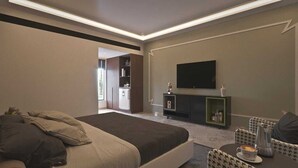 A modern hotel room with a large bed, a flat-screen TV mounted on the wall, a small seating area with a table and chairs, and a kitchenette in the background. - Sawariya The Boutique Resort (Mahasi)