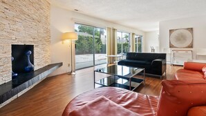 A modern living room with a fireplace, a glass coffee table, a black sofa, and a red leather couch.