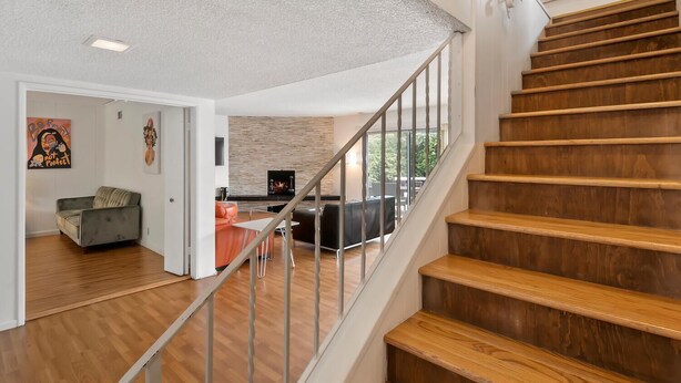 A modern interior with a wooden staircase, a living area with a sofa and a TV, and a kitchen visible through an open door.