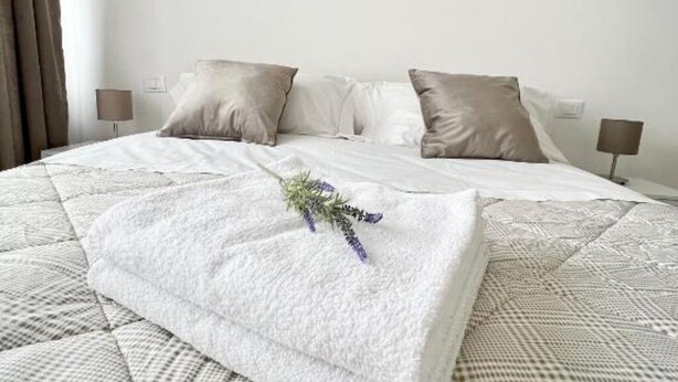 A neatly made bed with a quilt, two pillows, and a decorative lavender sprig.