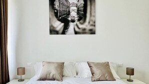 A neatly made bed with a patterned bedspread, two bedside tables with lamps, and a framed black and white photo of a canal on the wall.