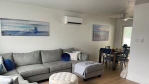 Un soggiorno moderno con un divano grigio, un pouf rotondo e un'area da pranzo con tavolo e sedie.