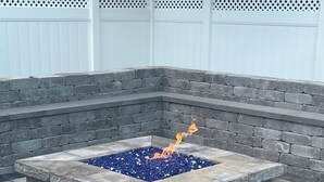 Fuoco in pietra con bordo in vetro blu, circondato da gradini in pietra e una recinzione bianca.