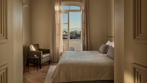 A hotel room with a large bed, a chair, a small table, and a view of the city through a window. - Amyth of Nicosia (Nicosia)