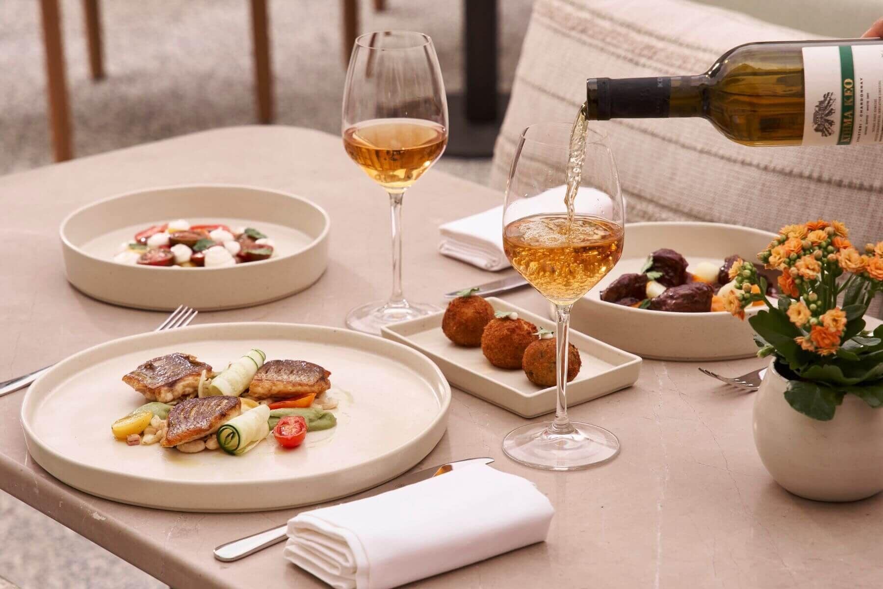 A table set with plates of food, glasses of wine, and a bottle being poured.