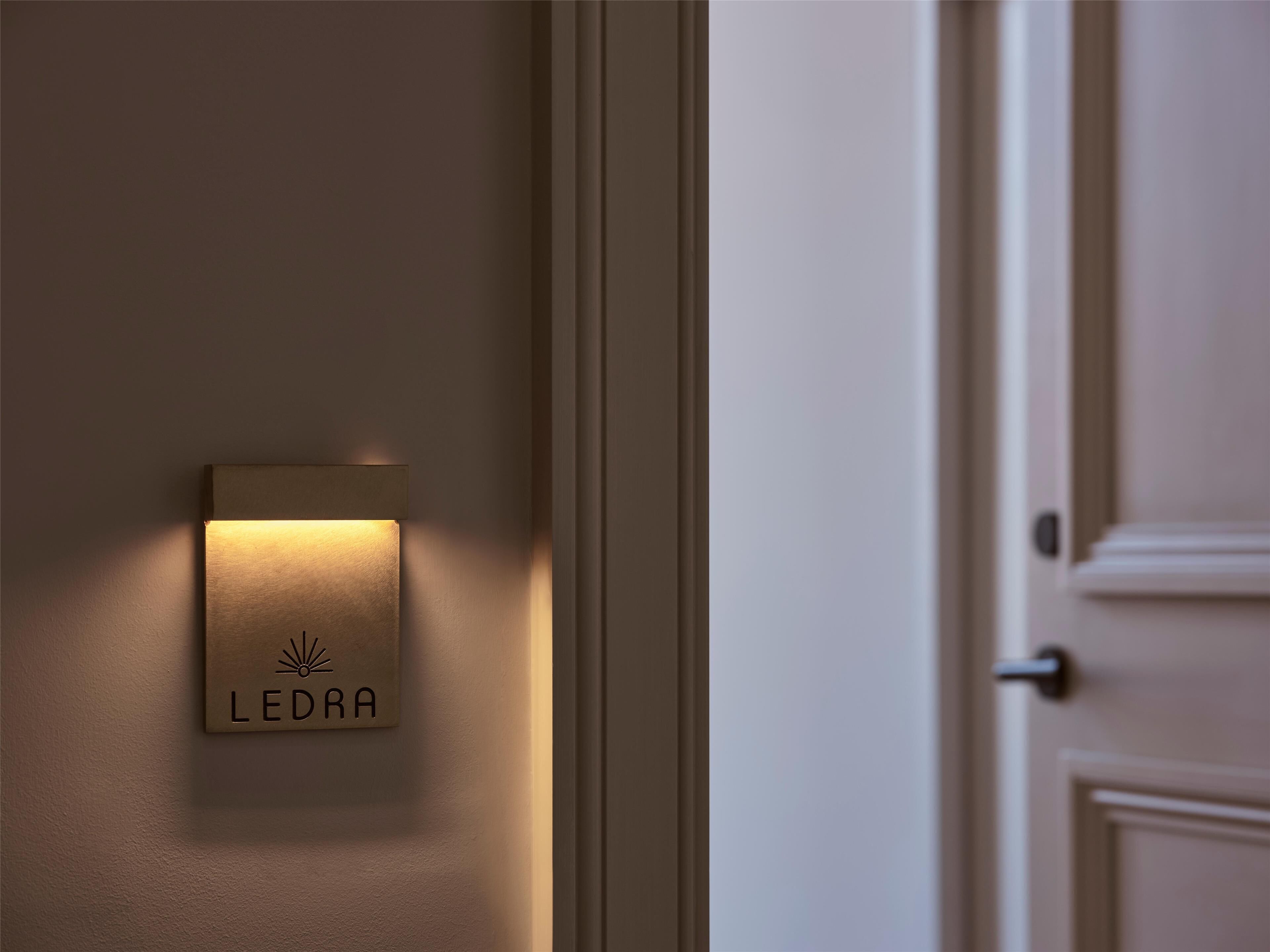 A wall-mounted LEDRA sign with a sunburst logo, mounted on a plain wall near a door.