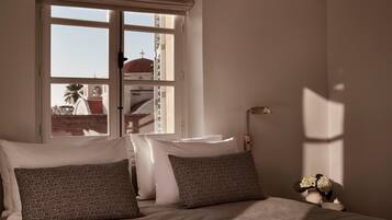 Una camera da letto con un letto, cuscini, un comodino, una lampada e una finestra vista edifici.
