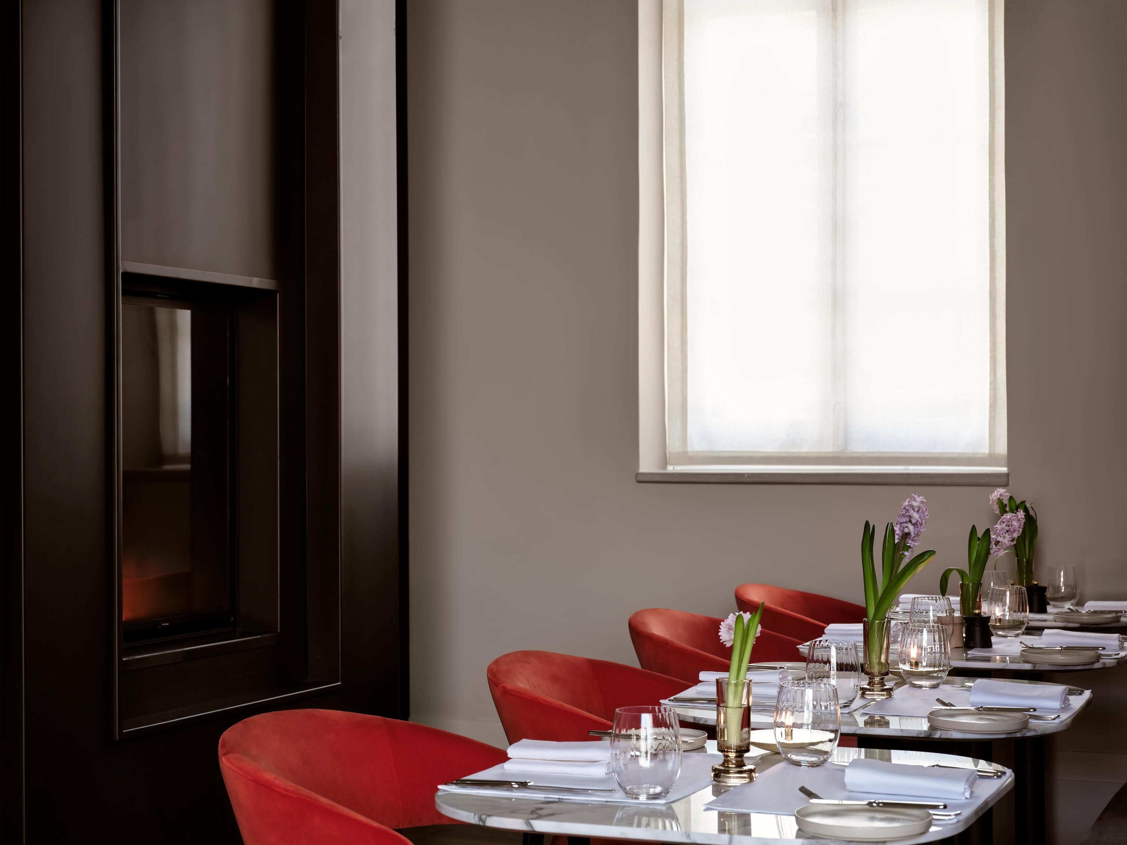 A dining area with a long table set for a meal, red chairs, and a window with natural light.