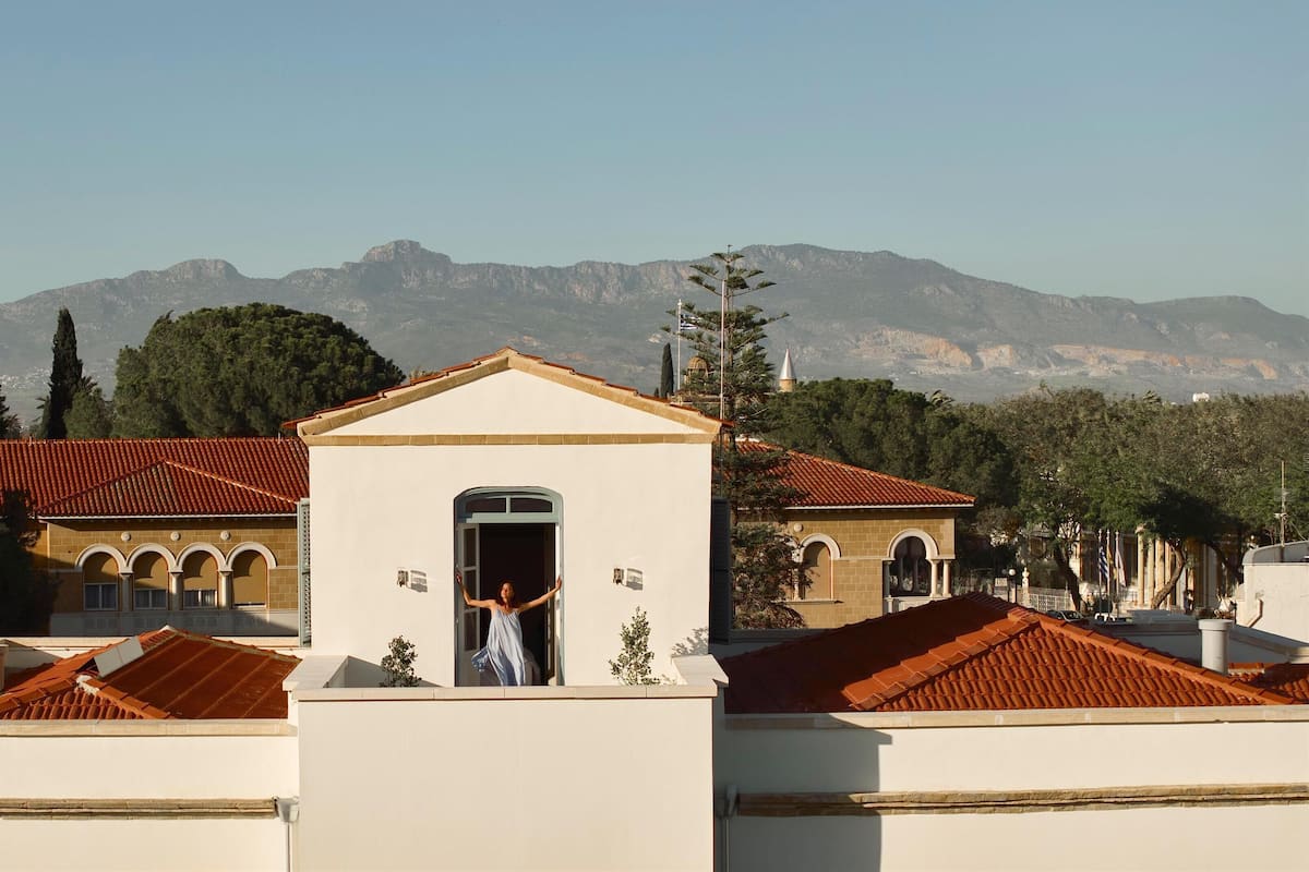 Un edificio con entrada central y ventanas arqueadas, rodeado de árboles y montañas.