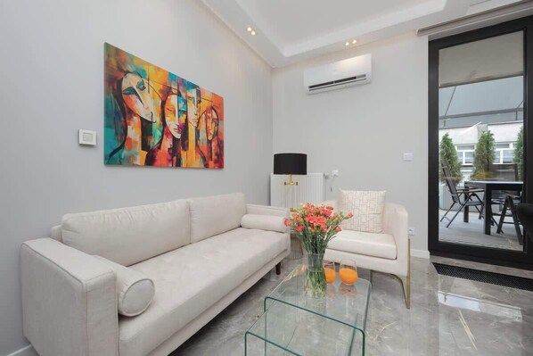 A modern living room with a white sofa, a glass coffee table with flowers, and a colorful abstract painting on the wall.