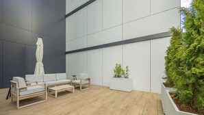 Un espacio al aire libre moderno con piso de madera, sofás blancos y una sombrilla blanca.