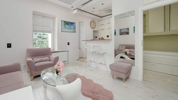 A modern living room with a glass coffee table, two sofas, a dining area with chairs, and a kitchen visible through an open door.