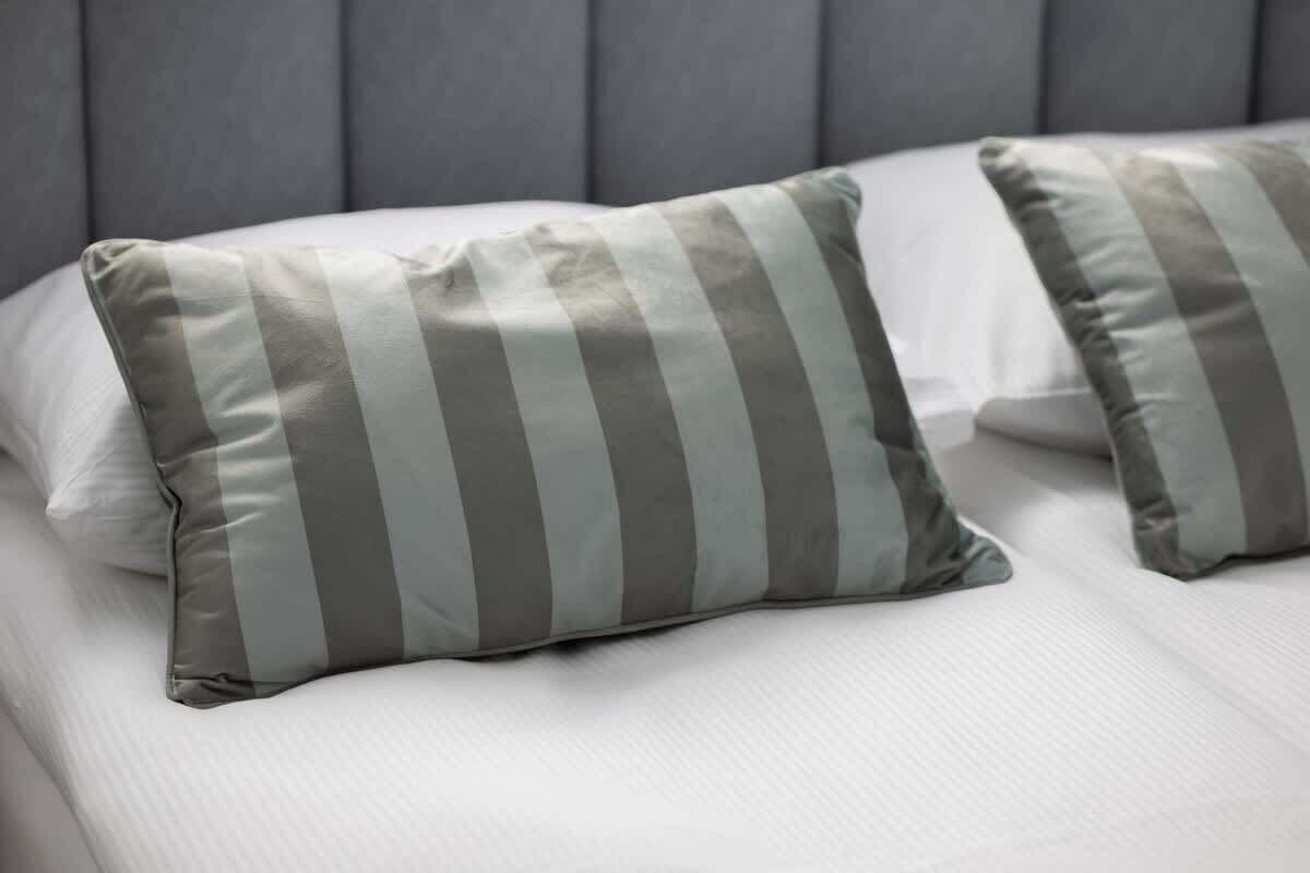 Ein Bett mit weißer Bettwäsche und zwei gestreiften Kissen.