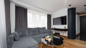 Una sala de estar moderna con un sofá seccional gris, una mesa de centro negra, un televisor de pantalla plana montado en la pared y piso de madera.
