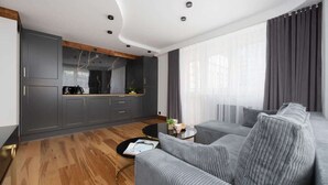 Una sala moderna con un sofá gris, una mesa de centro y una cocina con armarios grises y techo de madera.