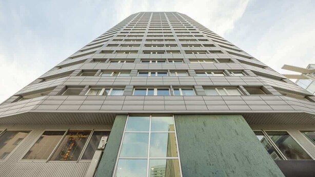 Un edificio alto y moderno con una fachada de ventanas enrejadas y una entrada destacada con puertas de vidrio.