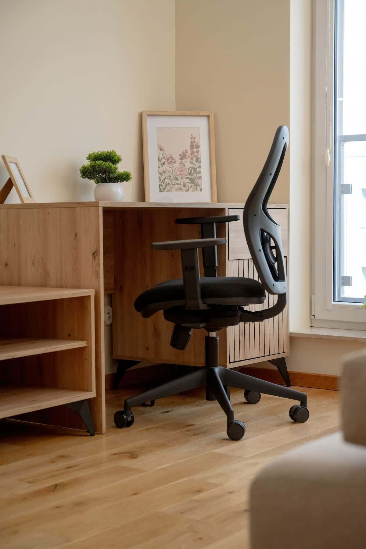 A modern office chair with wheels, a wooden desk, a framed picture, and a small potted plant.