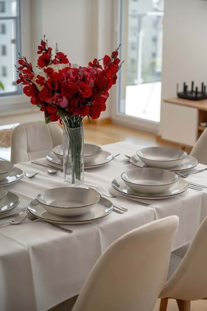 Une table à manger dressée avec des assiettes, des couverts et un vase rempli de fleurs rouges.
