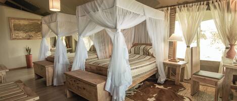 A four-poster canopy bed with a wooden headboard, a wooden bench, a small table, and a lamp.