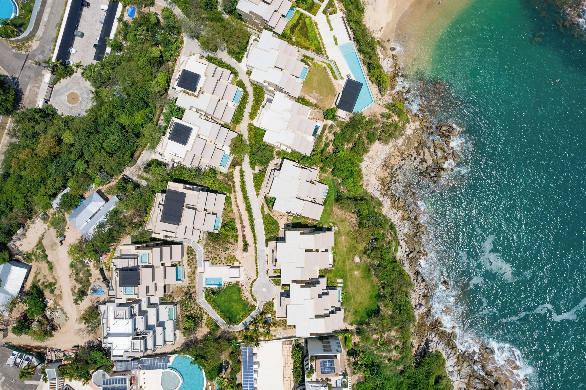 An aerial view of a coastal resort with multiple buildings, a beach, and a rocky shoreline.