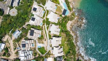 An aerial view of a coastal resort with multiple buildings, a beach, and a rocky shoreline.