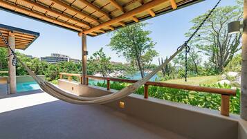 A hammock on a balcony overlooking a pool and lush greenery, with a view of distant buildings.
