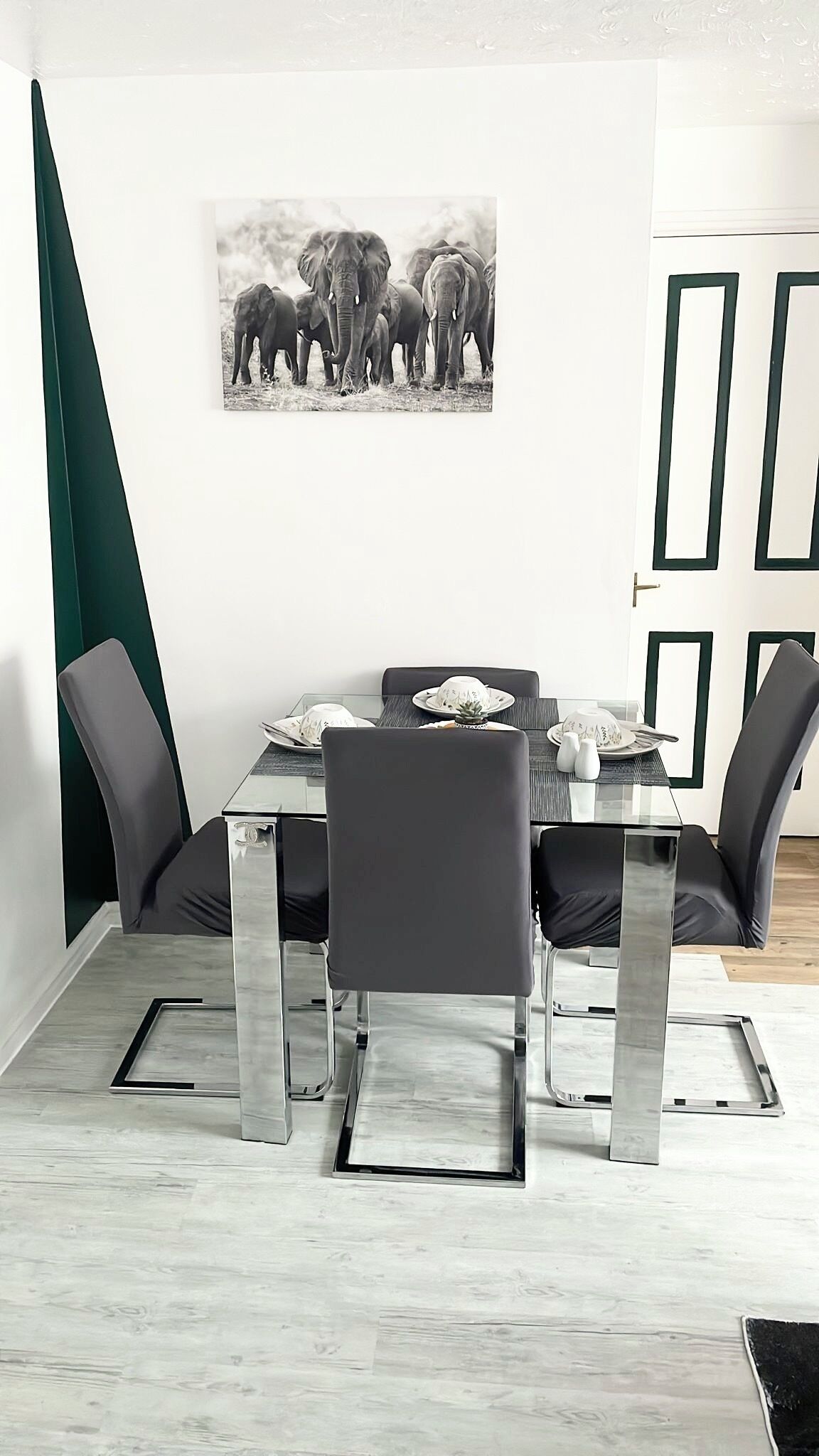 A dining area with a rectangular table, four chairs, and a framed picture of elephants on the wall.