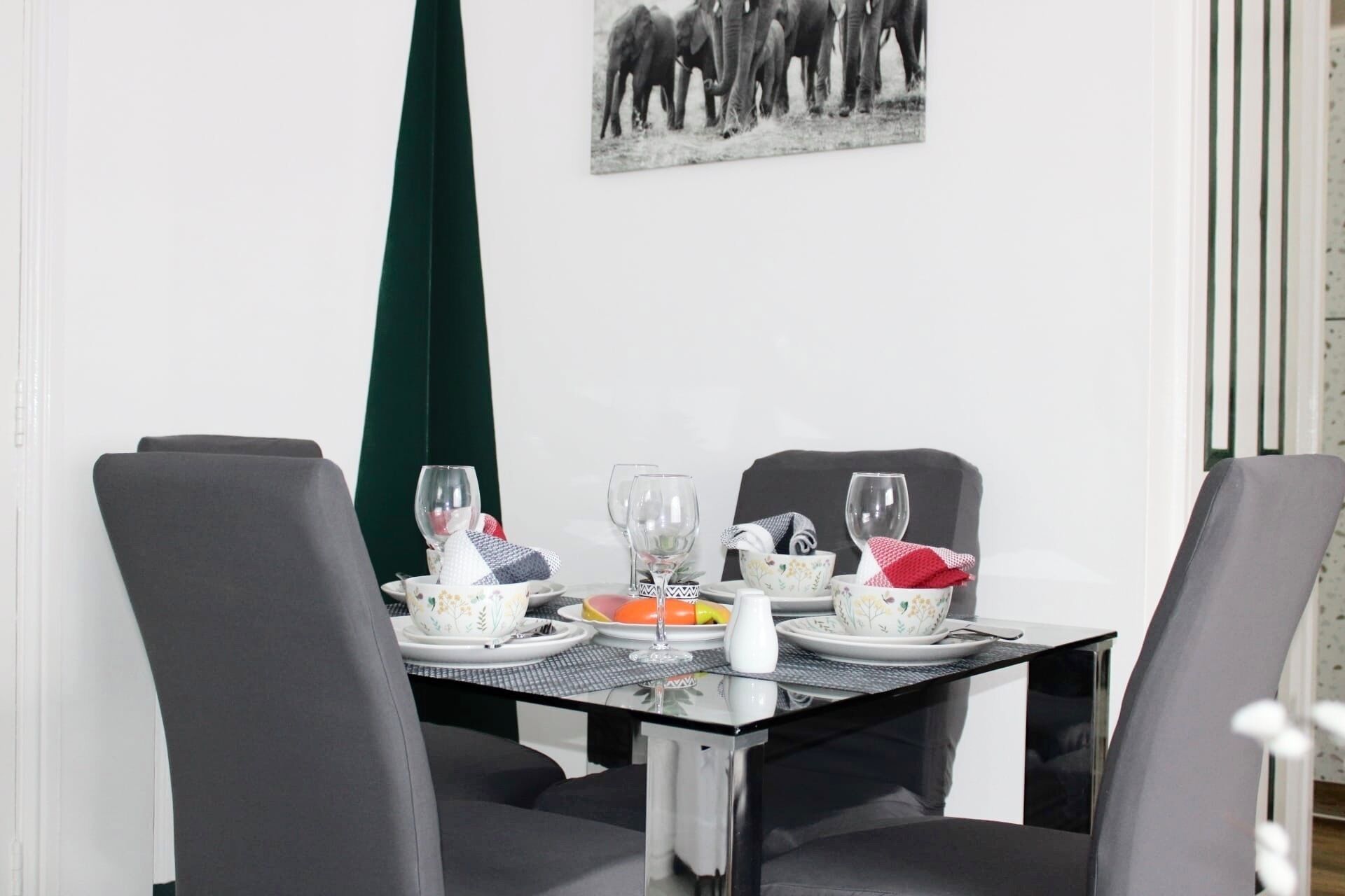 Une table à manger mise pour quatre personnes, avec des chaises, une nappe noire et un tableau encadré accroché au mur.