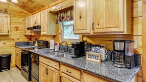 A wooden cabin kitchen with granite countertops, a coffee station, and a window with curtains. - 2 Mi to Dtwn Gatlinburg: 'crescent Claw Cabin!' (Gatlinburg)