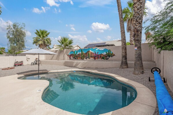 A swimming pool with a mural, palm trees, and a covered area with a striped umbrella.