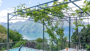 A terrace with a pool, a table with coffee cups, and a view of a lake and mountains. - Glicine by Interhome (Varenna)