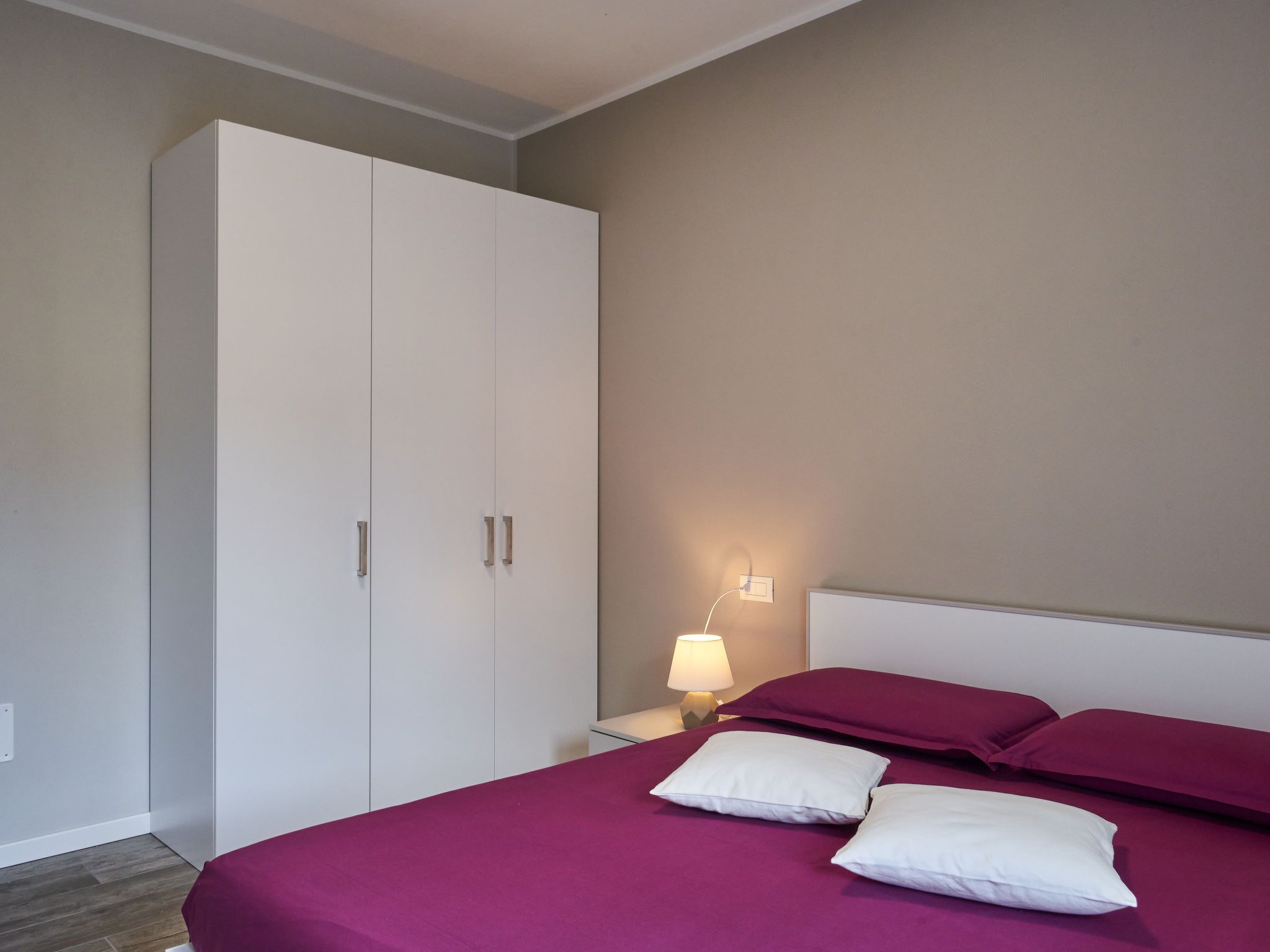 A bedroom with a bed, a wardrobe, and a nightstand with a lamp.