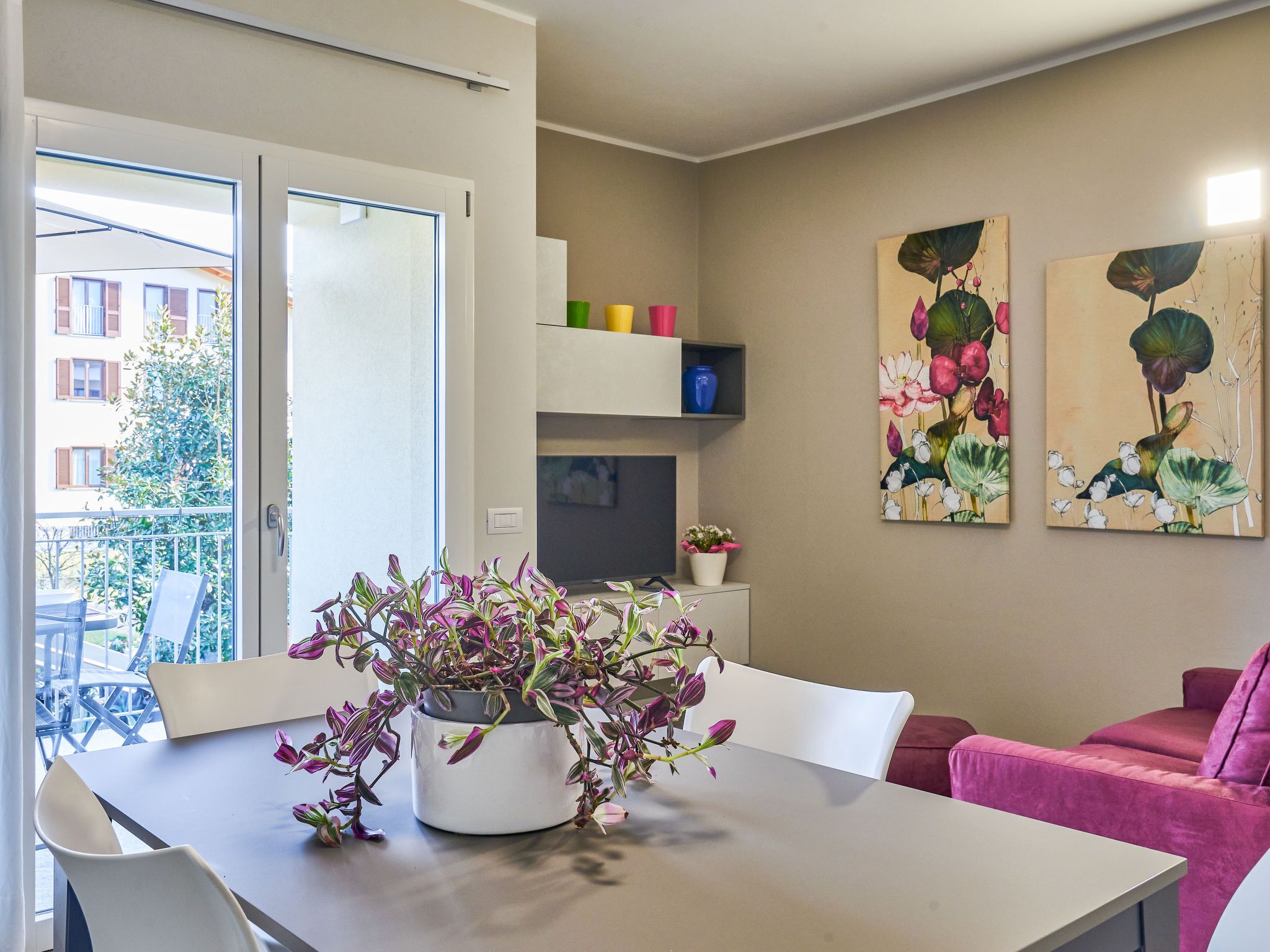 A dining area with a table, chairs, a potted plant, and artwork on the wall.