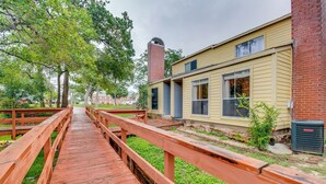A wooden deck leading to a building with a brick chimney, windows, and a small garden area. - College Station Gem w/ Pool Access Near University (College Station)