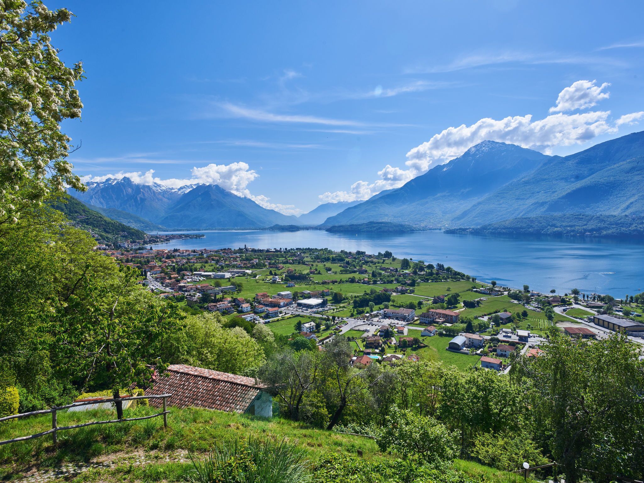 A panoramic view of a lakeside town with mountains in the background, featuring a mix of residential and commercial buildings.