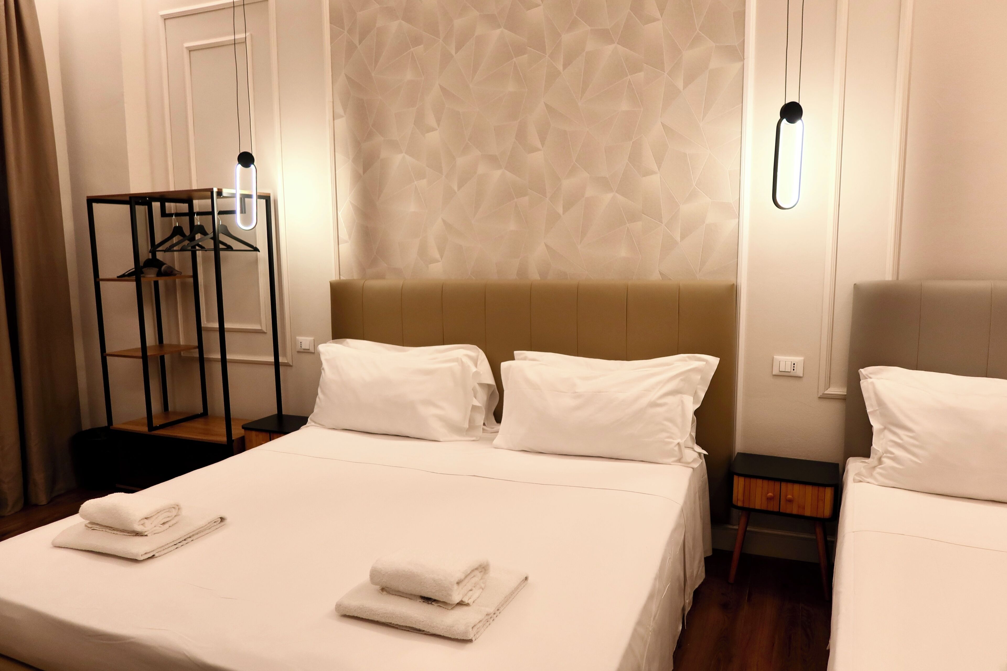 Une chambre d’hôtel avec un grand lit, deux tables de chevet, une armoire et un luminaire suspendu.