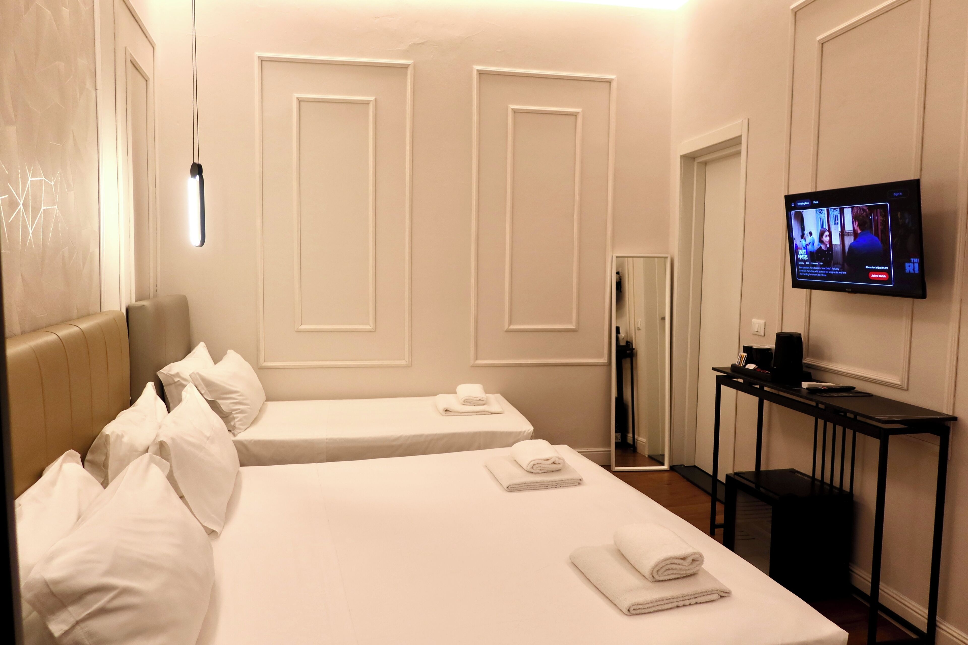 Habitación de hotel con dos camas, un televisor en la pared y una mesita con cafetera.