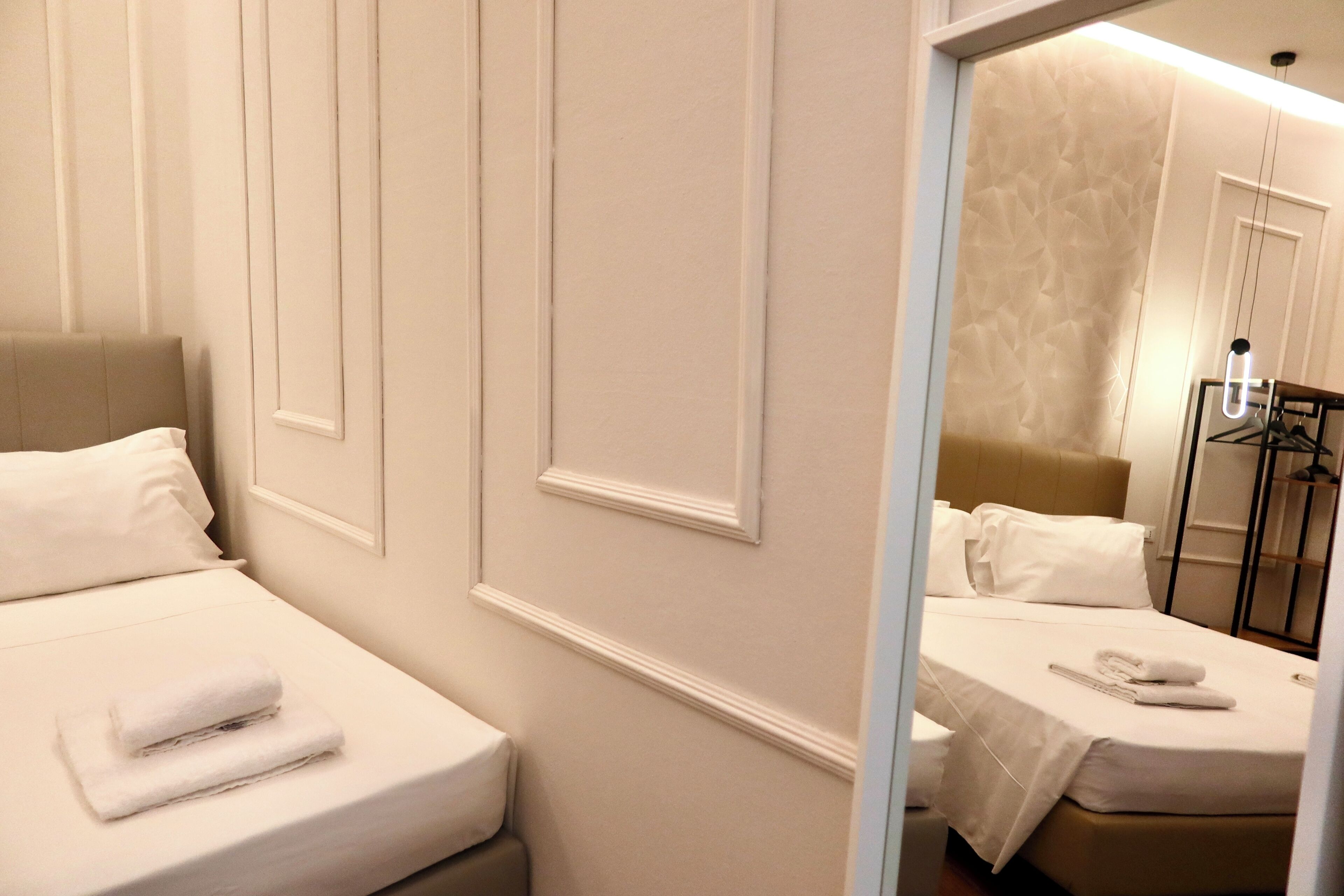 A hotel room with two beds, one with a headboard and the other with a plain headboard. Both beds have white linens and pillows.
