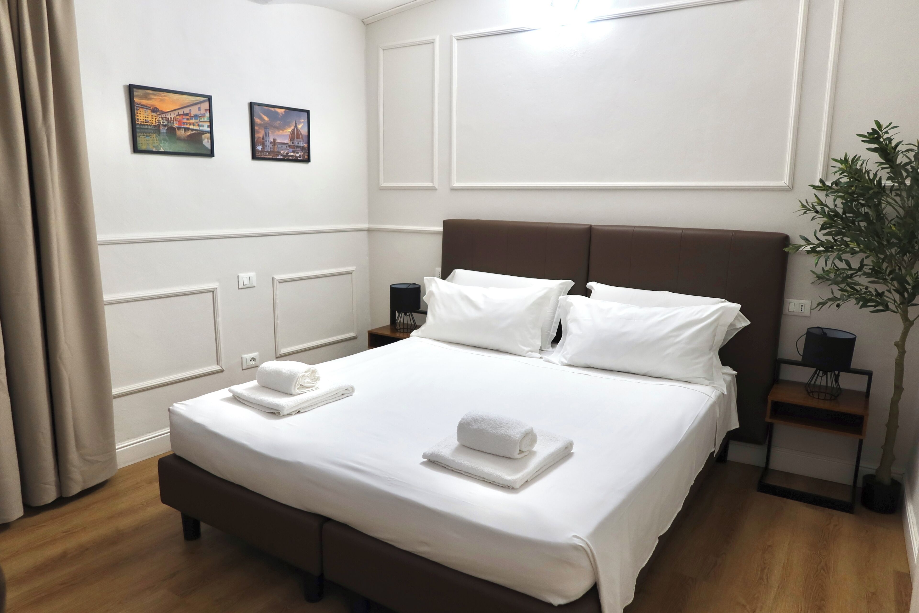 A neatly made bed with white linens and two towels, a brown headboard, and a small bedside table with a lamp.