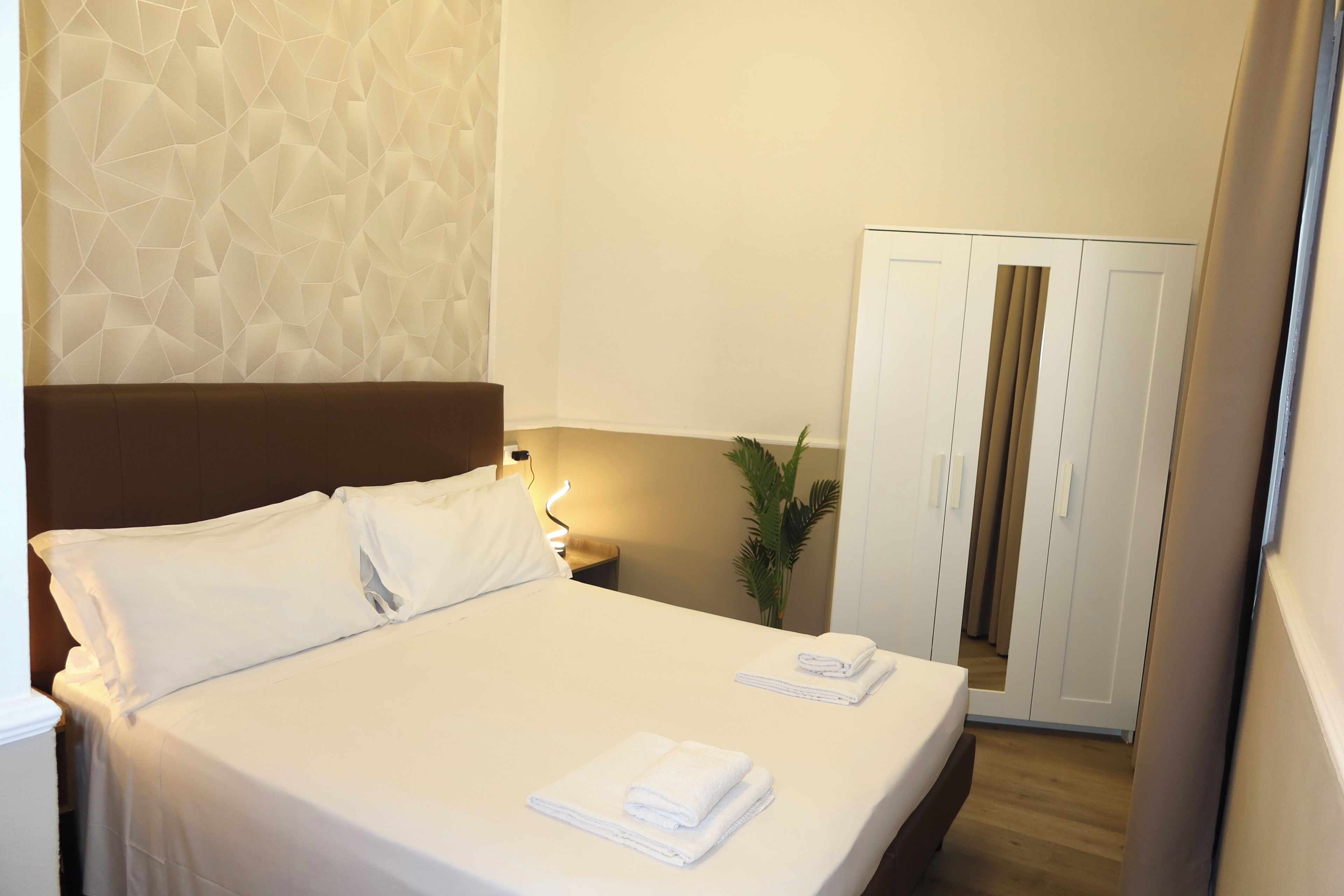 A neatly made bed with white linens and towels, a bedside lamp, and a wardrobe with sliding doors.