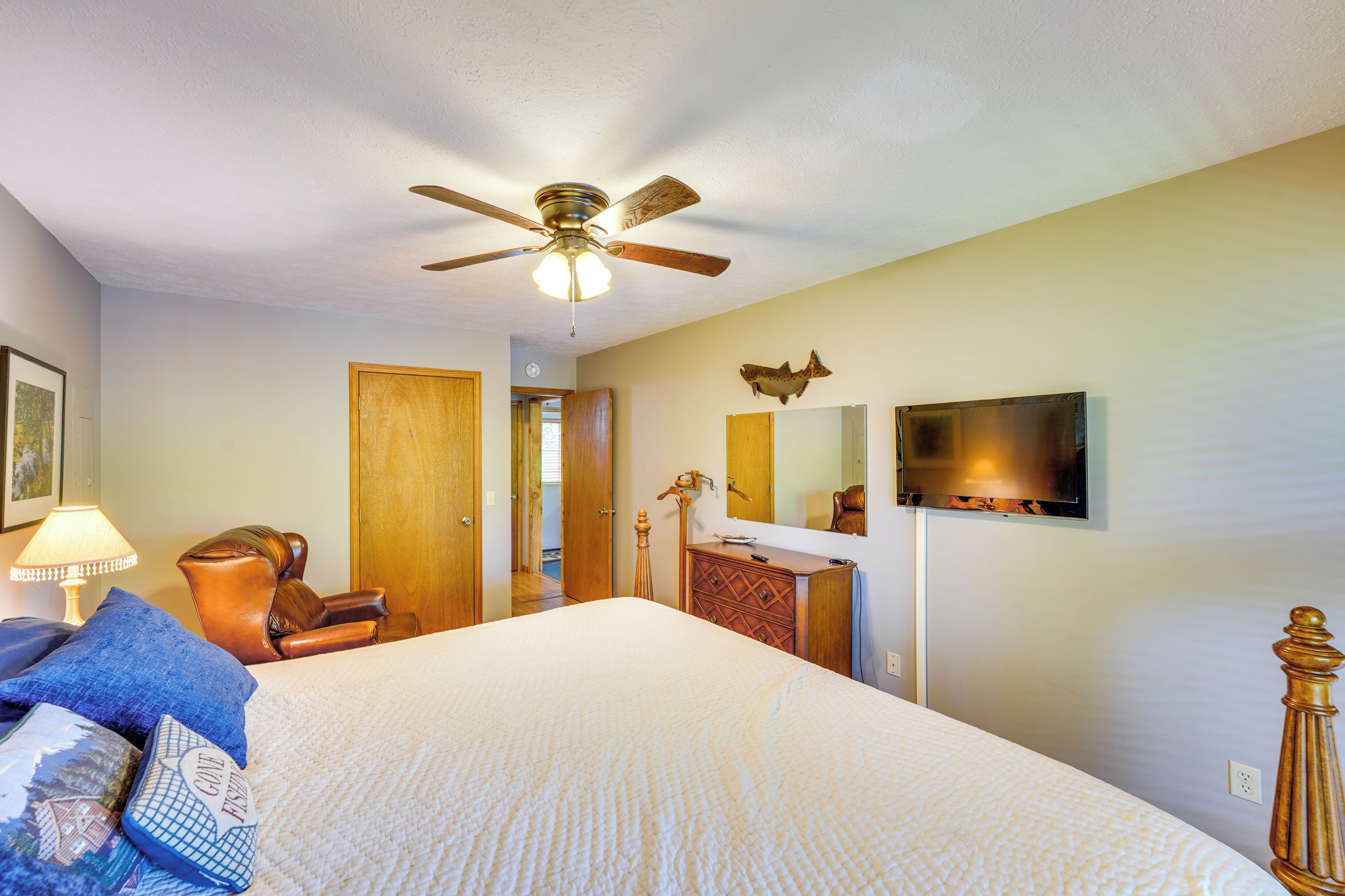 A bedroom with a bed, a ceiling fan, a dresser, a mirror, and a television.