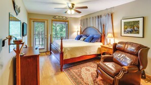 A bedroom with a bed, a wooden dresser, a leather armchair, a ceiling fan, and a window with curtains. - Flippin Home w/ Fire Pit: Walk to White River! (Flippin)