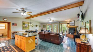 A spacious living area with a large brown leather sofa, a wooden island with a sink, and a dining area with chairs. - Flippin Home w/ Fire Pit: Walk to White River! (Flippin)