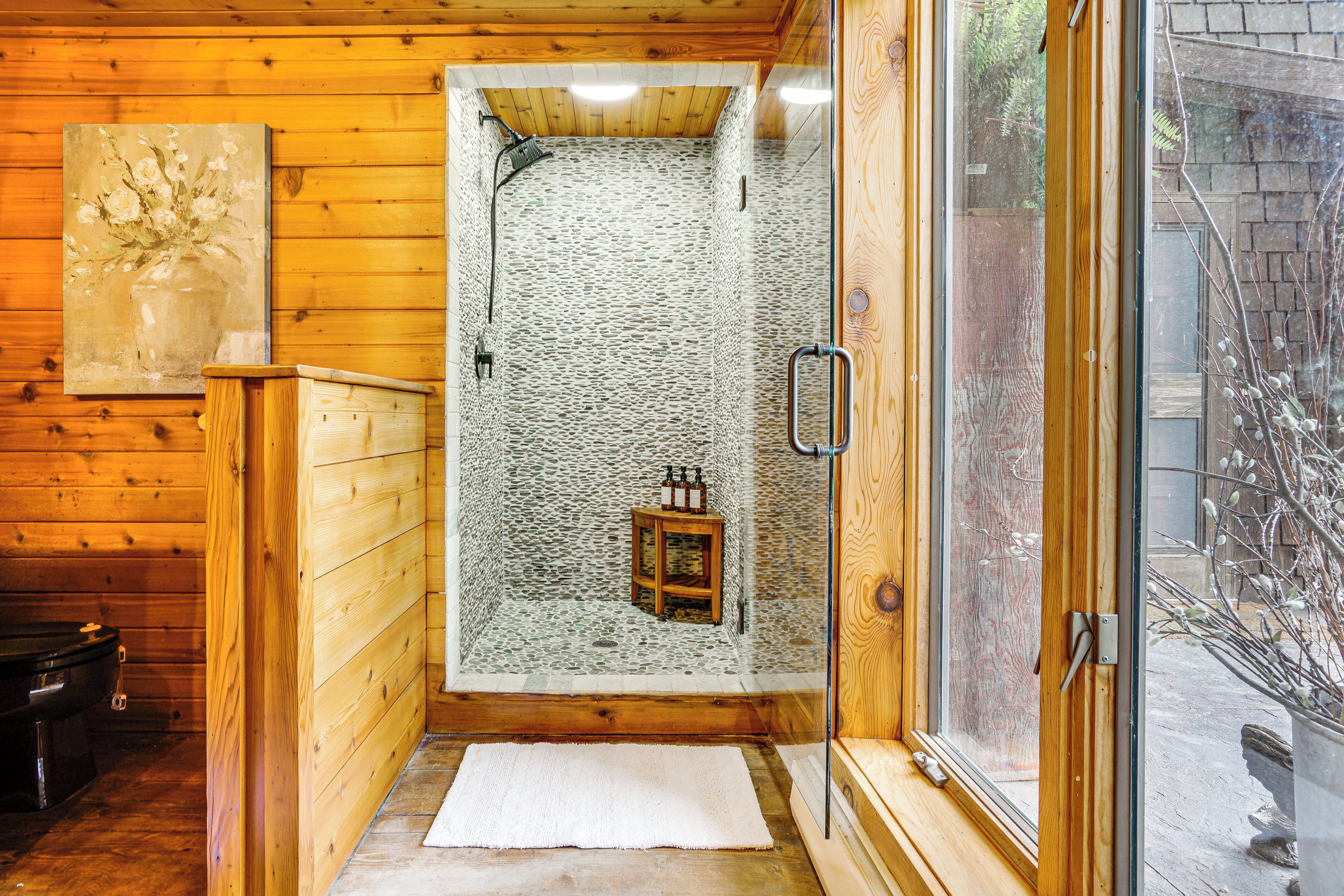 A wooden cabin with a stone shower, a wooden bench, and a small wooden stool.