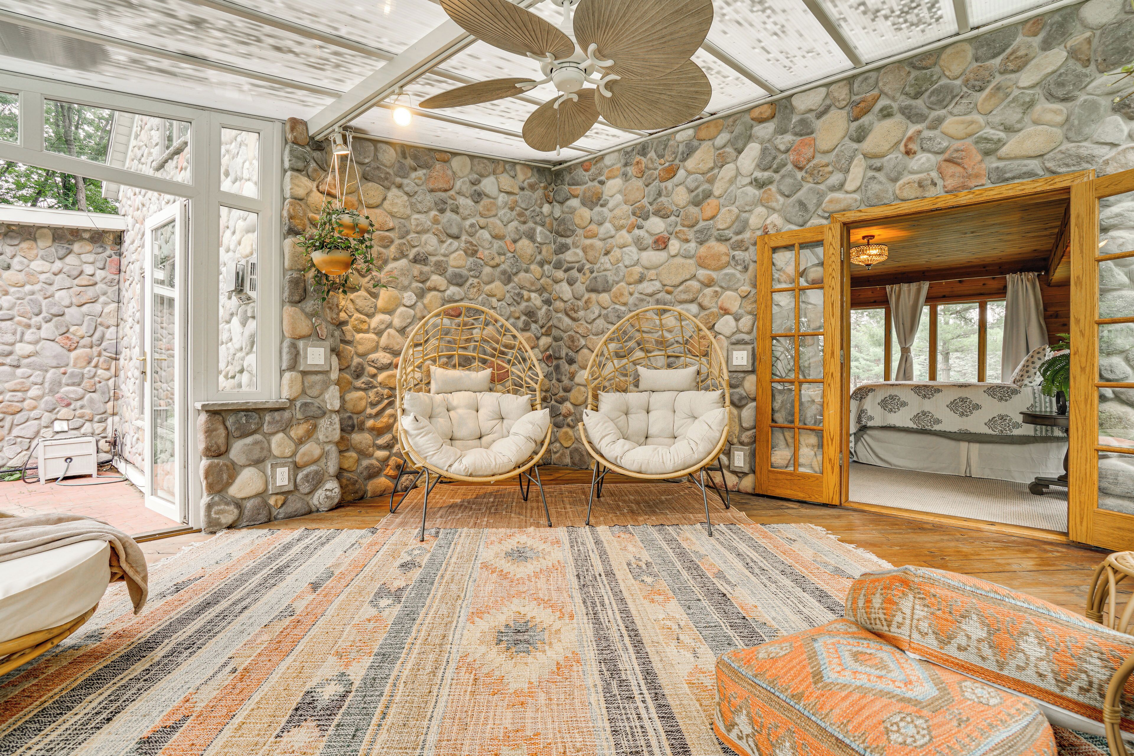 A room with stone walls, wicker chairs, a patterned rug, and a ceiling fan.
