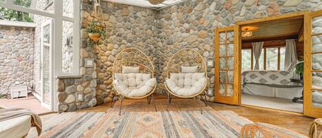 A room with stone walls, wicker chairs, a patterned rug, and a ceiling fan.